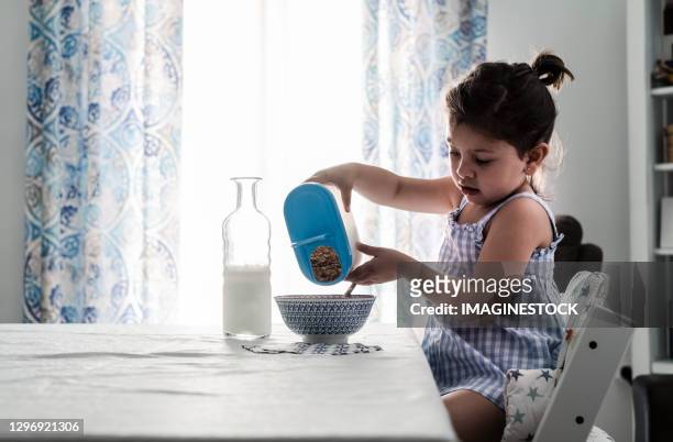 little girl preparing the cereal-milk breakfast in the dining room at home - toddler milk stock-fotos und bilder