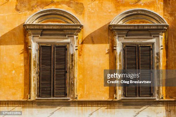 yellow shabby facade of old european building with wooden vintage rustic shutters on windows - facade blinds stock pictures, royalty-free photos & images