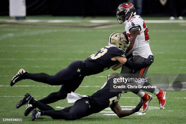 Leonard Fournette of the Tampa Bay Buccaneers gets tackled by Zack Baun and Malcolm Jenkins of the New Orleans Saints in the NFC Divisional Playoff...