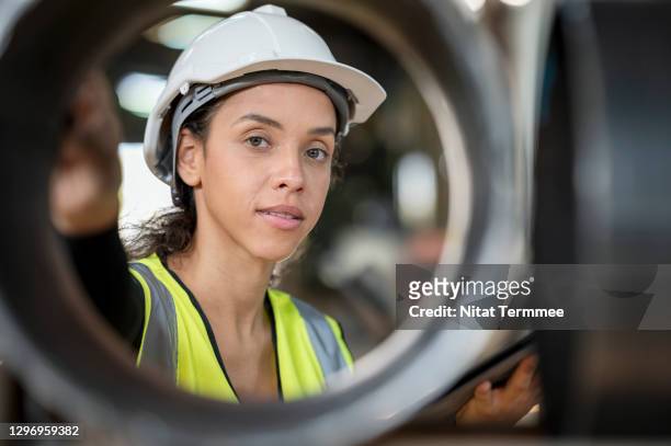 portrait of female engineer examining surface of silver steel pipes at factory warehouse. - variable schärfentiefe stock-fotos und bilder