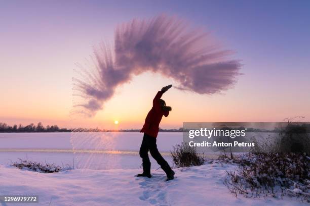 man pours boiling water into the air in the bitter cold. outdoor winter fun - unusual imagens e fotografias de stock