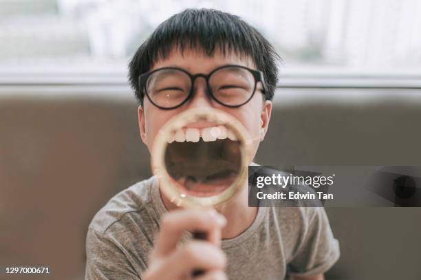 asiático chino adolescente niño sonrisa zoom cuidado de dientes sosteniendo lupa en sus dientes mirando el humor de la cámara - big lips fotografías e imágenes de stock