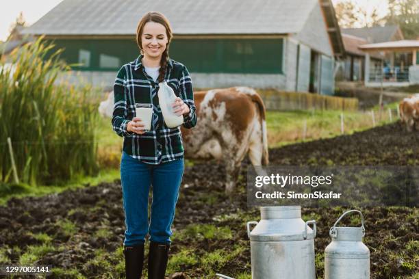 junge frau hält milchflasche mit glas auf milchviehbetrieb - happy cow stock-fotos und bilder