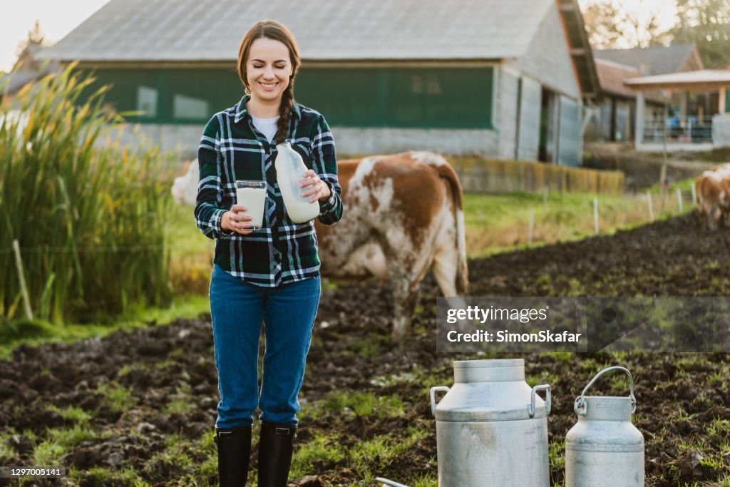 Young woman holding milk bottle with glass on dairyfarm