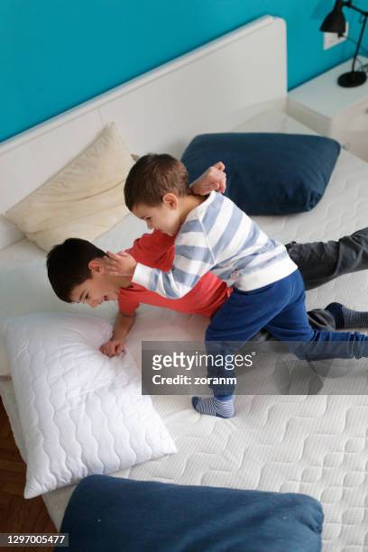 two little brothers wrestling on empty bed for fun, play time during house move - boys wrestling stock pictures, royalty-free photos & images