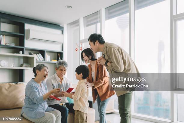 asian chinese grandparents giving out red packets angpao to grandson during chinese new year at home - patrick grant stock pictures, royalty-free photos & images