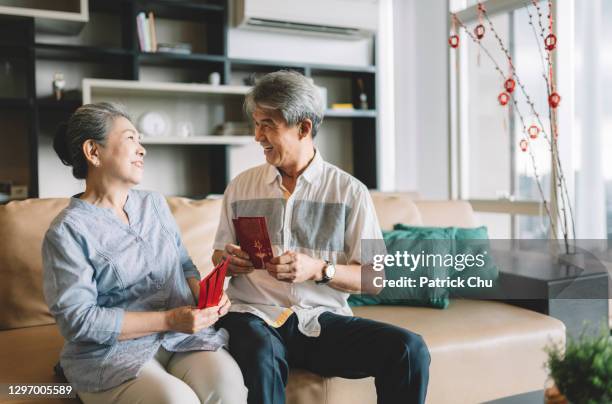 asian chinese grandparents talking and smiling while holding red envelope celebrating chinese new year at home - 70 year male stock pictures, royalty-free photos & images