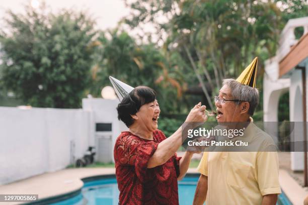 laughing asian chinese grandma feeding cake to grandpa on his birthday celebration - its about love celebration stock pictures, royalty-free photos & images