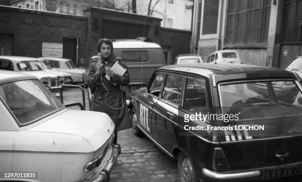 Le journaliste Michel Drucker tenant un micro debout à côté de la voiture technique de la radio RTL en novembre 1975, Paris, France.