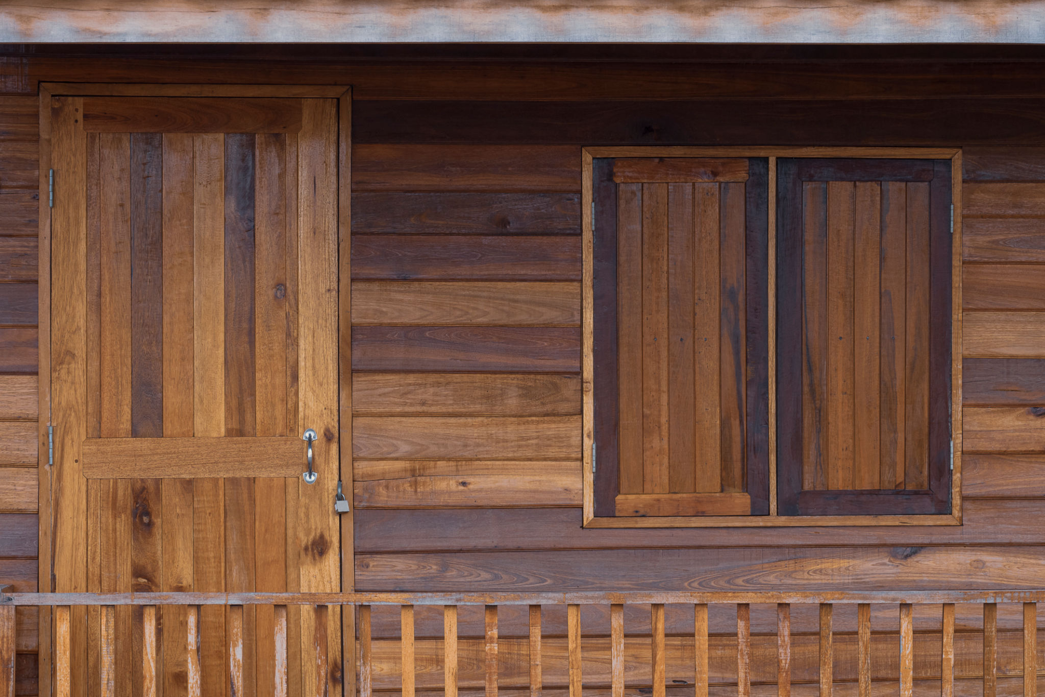 Front view of wooden door and window with porch railing made from recycled old wood panels Front view of wooden door and window with porch railing made from recycled old wood panels