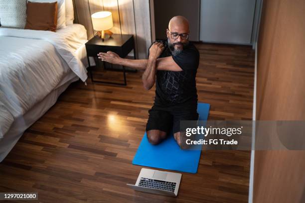 mature man exercising at home - watching virtual exercise class on laptop - covid-19 guidance stock pictures, royalty-free photos & images