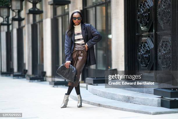 Emilie Joseph wears sunglasses, a dark navy blue striped oversized blazer jacket from Frankie Shop, a white wool turtleneck pullover with printed...