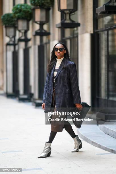 Emilie Joseph wears sunglasses, a dark navy blue striped oversized blazer jacket from Frankie Shop, a white wool turtleneck pullover with printed...