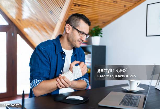 businessman with bandaged wrist is suffering from wrist joint pain at home office. office syndrome hand pain by occupational disease. - bandage stock pictures, royalty-free photos & images