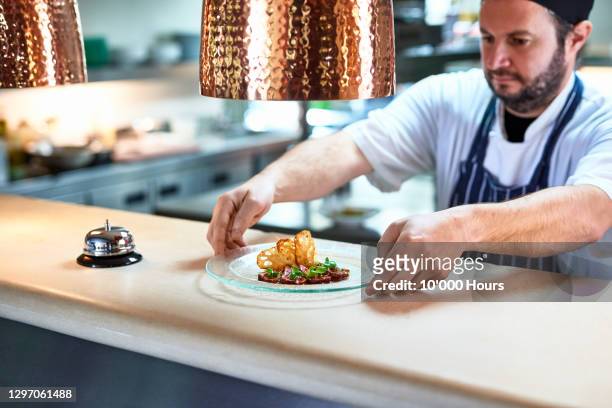 chef placing plate of food on service counter - piatto di portata foto e immagini stock