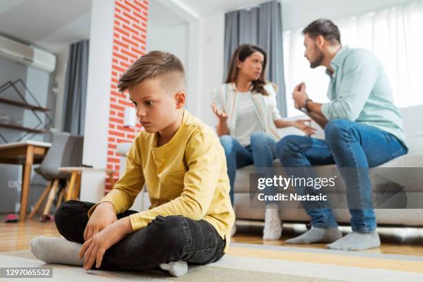 trauriger junge, der seinen eltern zuhört und nach unten schaut - streiten stock-fotos und bilder
