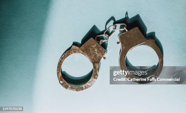 simple conceptual image of silver handcuffs on blue surface - handcuffs imagens e fotografias de stock