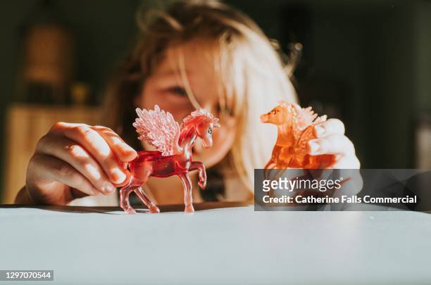 little girl holds two plastic unicorns on a soft surface - figurines stock-fotos und bilder