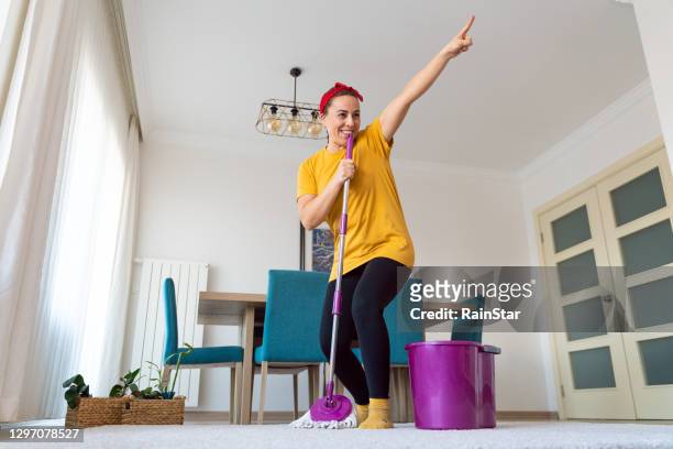 jeune femme rêveuse qui commence soudainement à chanter utilisant la vadrouille dans sa main comme microphone tout en nettoyant le plancher - cleaning home photos et images de collection