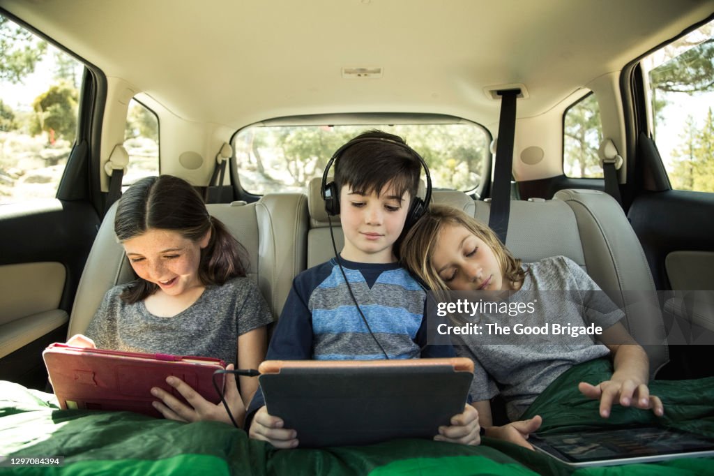 Siblings using digital tablet in back seat of car on road trip