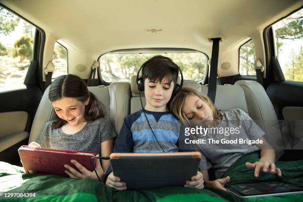 siblings using digital tablet in back seat of car on road trip - children on a tablet stockfoto's en -beelden