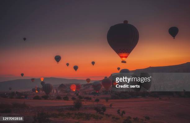 hot air balloons flying over rock formations at sunrise in cappadocia, goreme, turkey - cave fire stock pictures, royalty-free photos & images