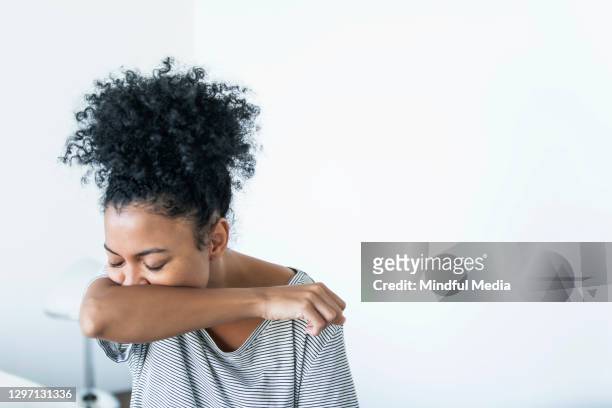 young woman coughing on elbow indoors - woman cough stock pictures, royalty-free photos & images