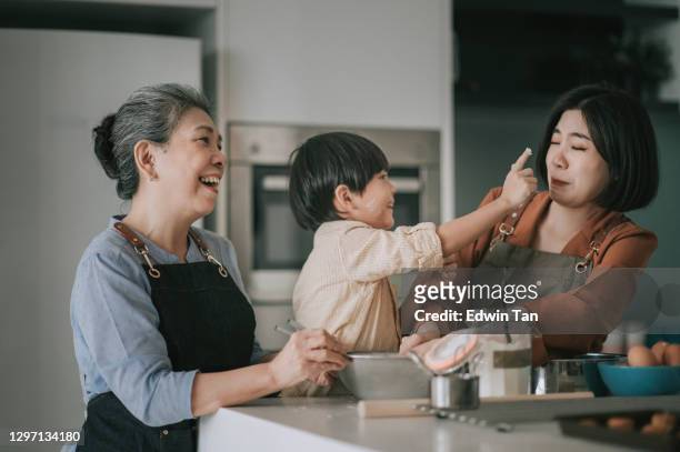 asiatische chinesische verspielte junge berührt seine mutter nase mit mehl beim backen in der küche mit seiner mutter und großmutter zusammen - asian granny pics stock-fotos und bilder