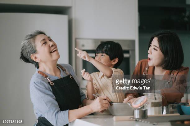 asian chinese playful boy touching his grandmother nose with flour during baking in kitchen with his mother and grandmother together - asian grandmother stock pictures, royalty-free photos & images