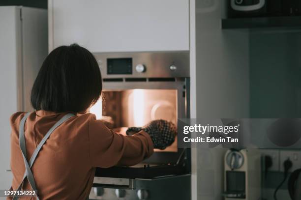 asian chinese young woman retrieving bakery item from electronic oven with protective glove - forma de bolo imagens e fotografias de stock