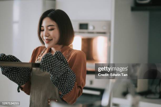 asiatische chinesische junge frau holt backwaren aus elektronischem ofen mit schutzhandschuh - woman back stock-fotos und bilder