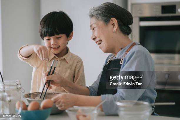 asiatische chinesische 6 jahre alten jungen hilft seiner großmutter zubereiten von essen mit mehl backen an der küchentheke zusammen - 6 7 years stock-fotos und bilder
