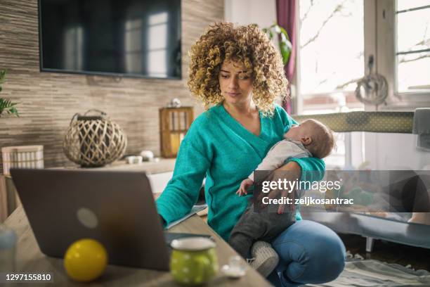 joven madre moderna con un bebé usando portátil en casa - leanincollection working mom fotografías e imágenes de stock