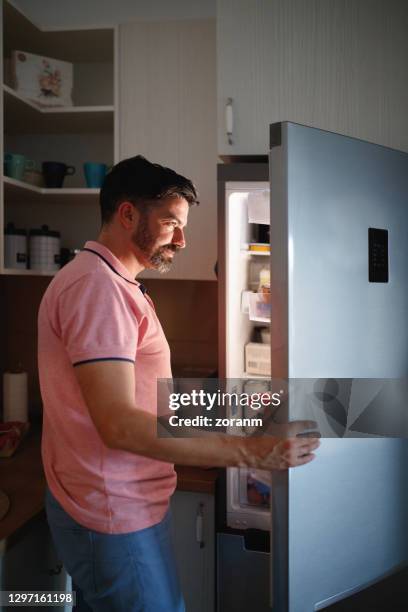 hombre con camiseta rosa mirando dentro del refrigerador y eligiendo comestibles - un solo hombre maduro fotografías e imágenes de stock