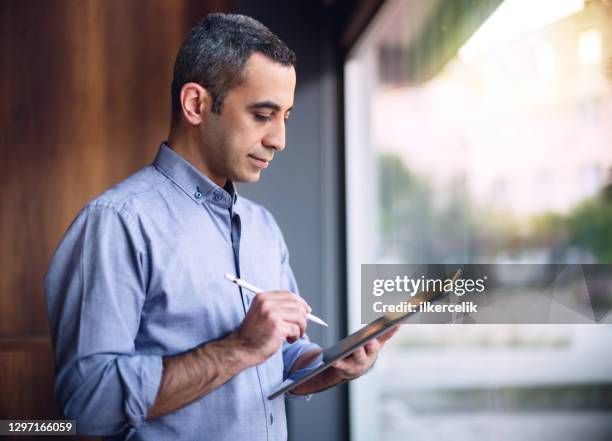 geschäftsmann in casual kleidung schreiben auf digitalen tablet mit stift in der nähe des fensters im büro - digital signature stock-fotos und bilder