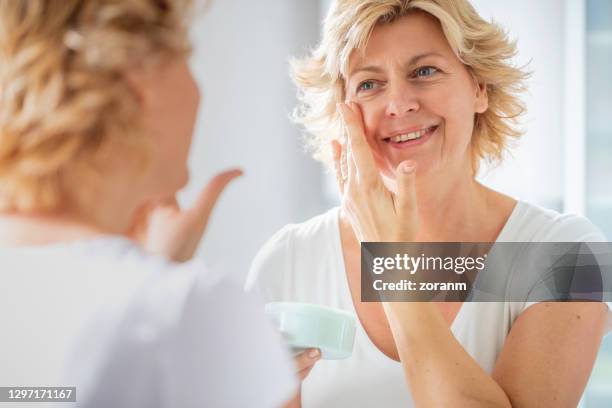 鏡の前で顔のクリームを着た陽気な女性 - 乳液 ストックフォトと画像