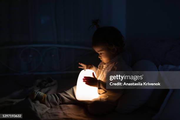 baby girl playing with children's nightlight on bed at night. - baby night stock-fotos und bilder