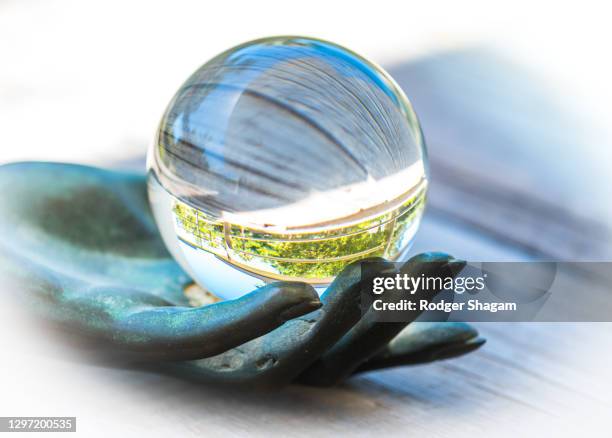 bronze hand holds a glass ball with the background showing an inverted image - glass sculpture stock pictures, royalty-free photos & images