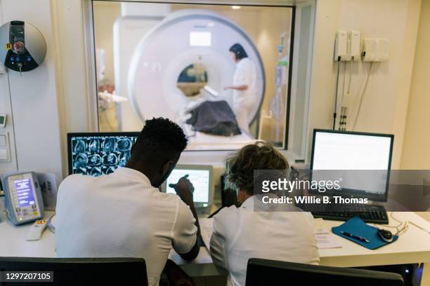 mri technicians watching from observation office as patient is prepared for scan - brain scan stock pictures, royalty-free photos & images