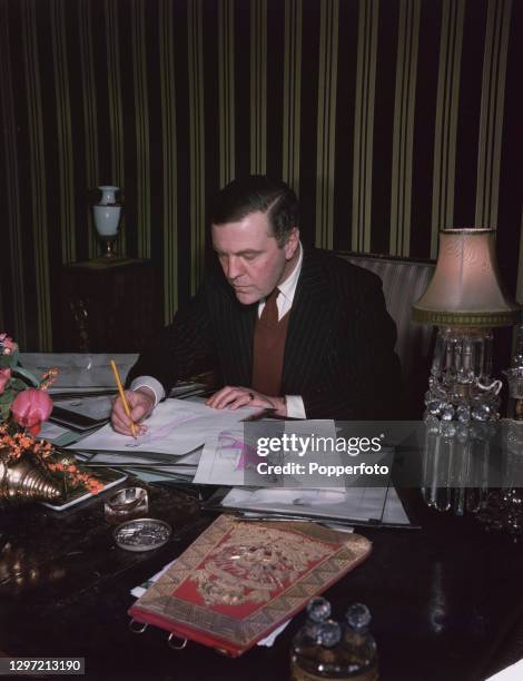 English fashion designer Norman Hartnell works on sketches of designs for the Queen's and Princesses wardrobe for the upcoming royal tour of South...