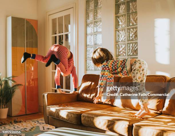 children bouncing on a brown leather sofa in a sunny domestic room - family jumping stock pictures, royalty-free photos & images