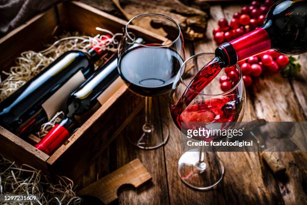 het gieten van rode wijn in een glas op rustieke houten lijst - wijnfles stockfoto's en -beelden