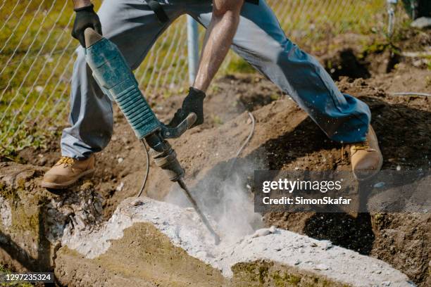 low section of worker drilling concrete block using jackhammer - jackhammer stock pictures, royalty-free photos & images