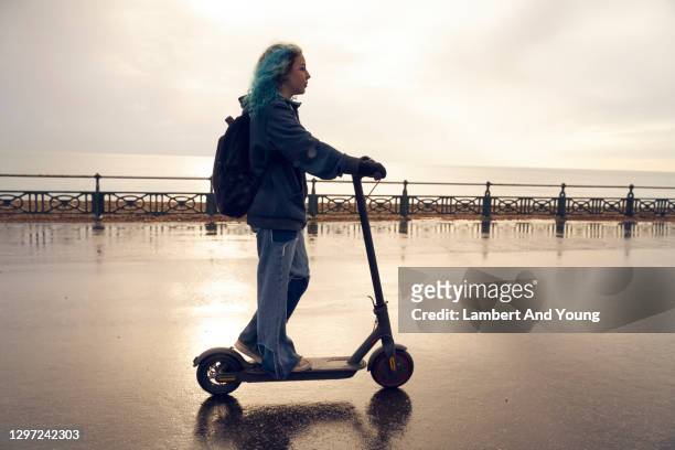 young woman riding an electric scooter along the coast with the sun behind her - young teen girl beach ストックフォトと画像