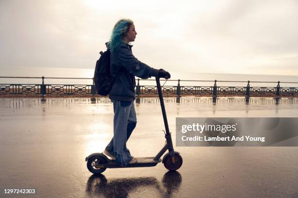 young woman riding an electric scooter along the coast with the sun behind her - girl riding scooter stock pictures, royalty-free photos & images