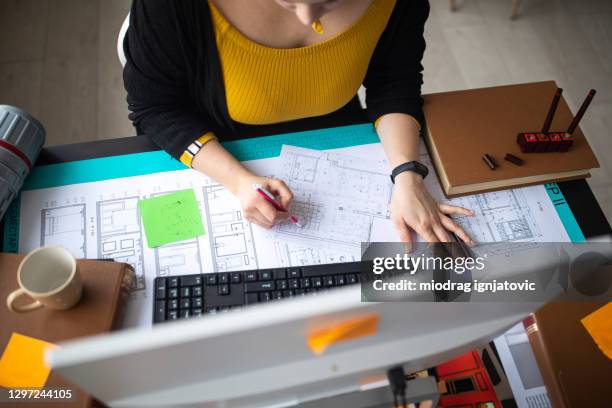 female architect drawing new ideas on blueprint while sitting at desk in office - sticky-notes-covering-computer-monitor stock pictures, royalty-free photos & images