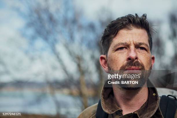 portrait of rugged handsome man with beard, contemplating life in outdoor landscape - macho stock pictures, royalty-free photos & images