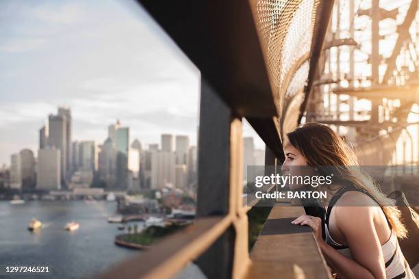 beautiful woman looks out across modern city from steel bridge - australia city lifestyle stock-fotos und bilder