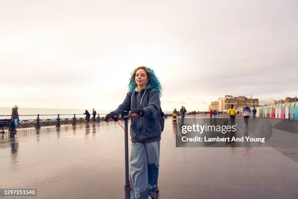 young woman commuting riding an electric scooter along the coast - seaside town stock pictures, royalty-free photos & images