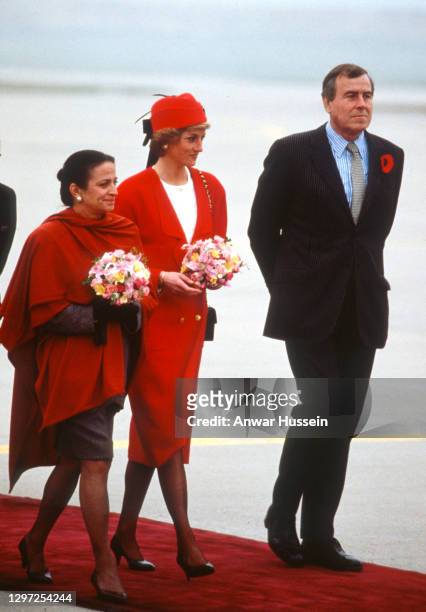 Diana, Princess of Wales, wearing a red coat with gold buttons and a matching hat designed by Chanel, stands between wife of French Prime Minister...